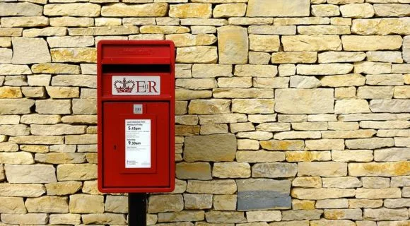 A red British post box in front of a beige brick wall