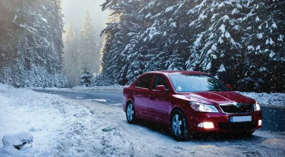 A red car parked on the side of the road in snow filled forest