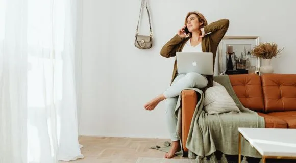 A woman sat on the edge of her sofa, on the phone looking concerned