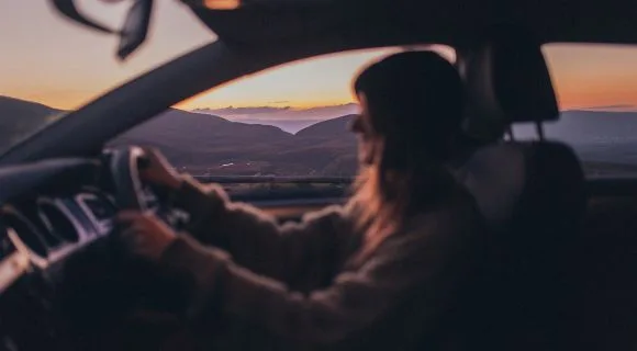 An out of focus side profile of someone driving as the sun sets