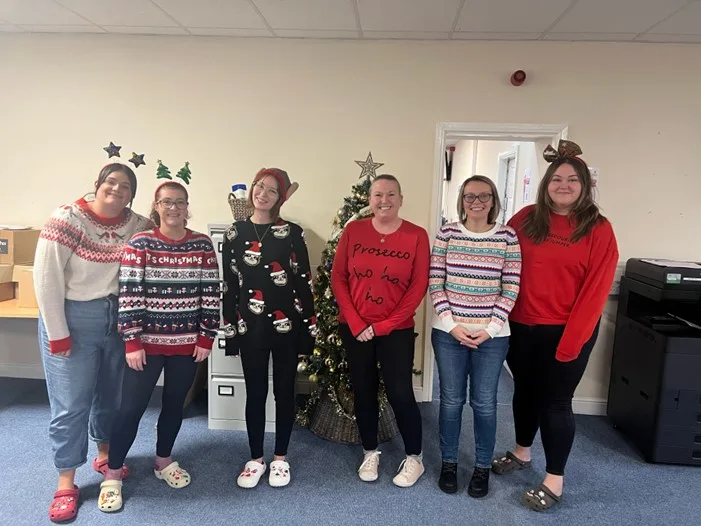 Staff members posing with festive sweaters in front of a Christmas tree