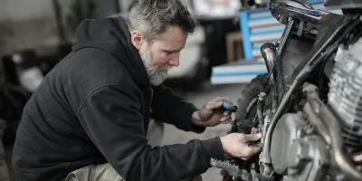 A mechanic fixing a motorbike, holding a screwdriver