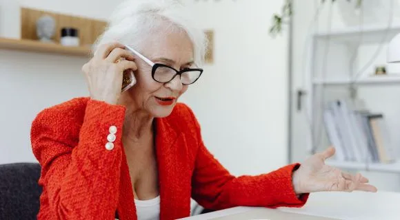 Older woman on the phone wearing a bright red blazer and lipstick
