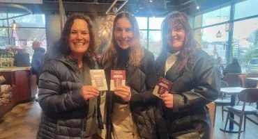 Three women dressed in black and beige smile while holding up their gift cards