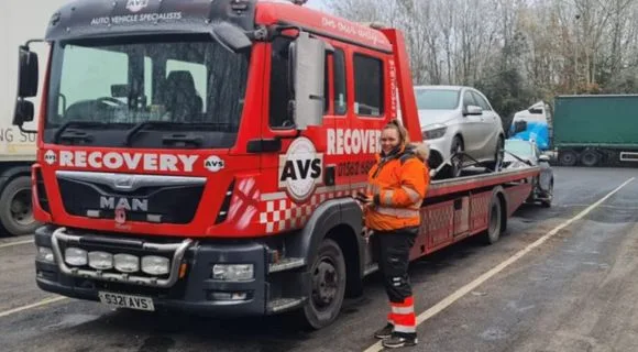 Recovery truck driver, Vicky, dressed in her orange high vis coat, stands near her truck
