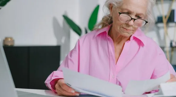A mature woman wearing a pink shirt, reading letters